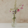 Glaskaraffe mit kleinen schwarzen Herzen als Vase mit rosa und violetten Blumen
