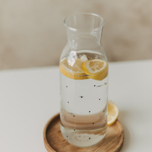 Glaskaraffe mit kleinen schwarzen Herzen, Wasser und schwimmenden Zitronenscheiben