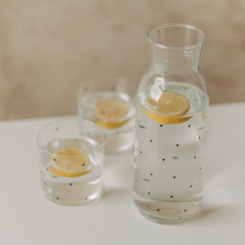 Karaffe und zwei Gläser mit kleinen schwarzen Herzen und Zitronenscheiben im Wasser
