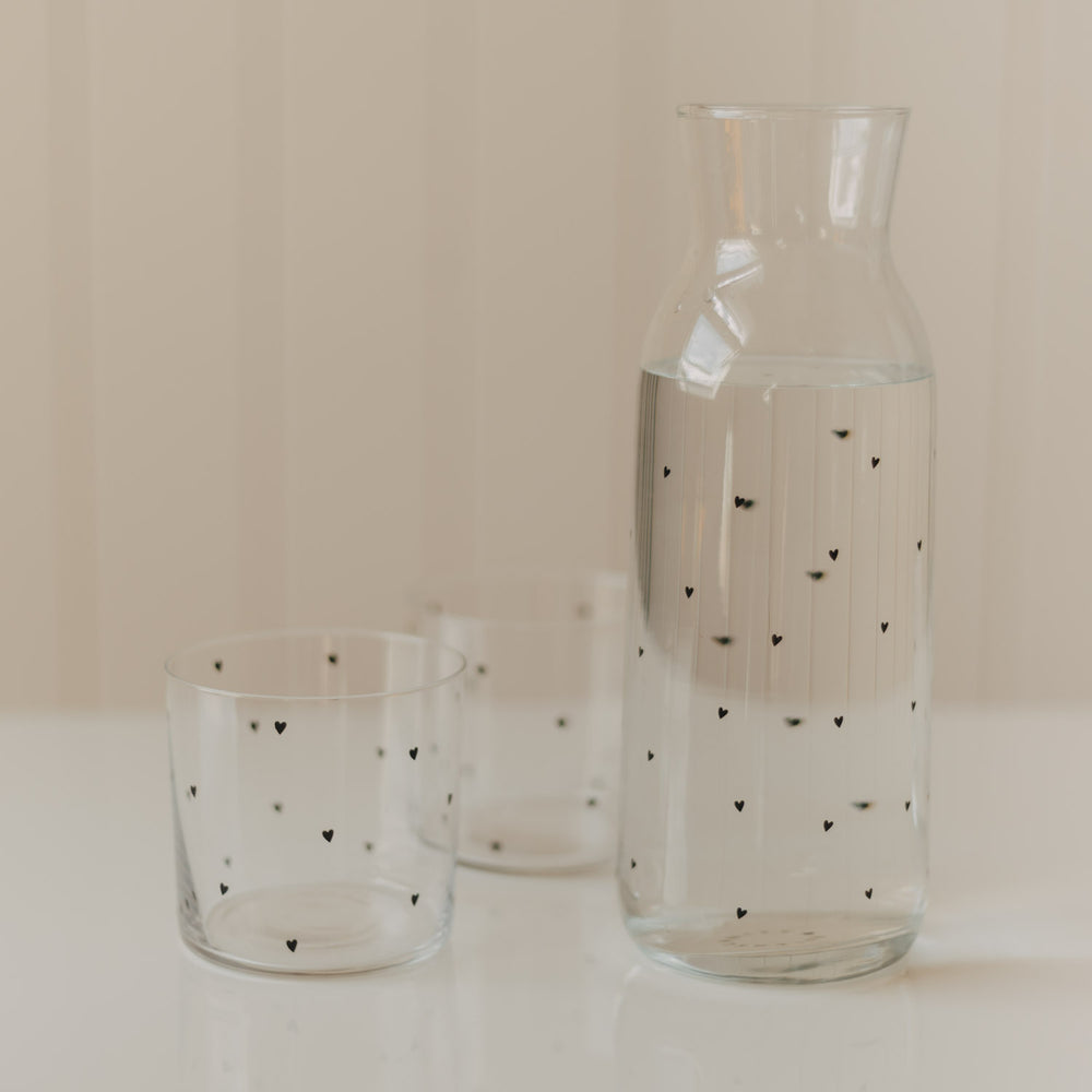 Glaskaraffe mit Wasser und zwei passenden Trinkgläsern mit kleinen schwarzen Herzen