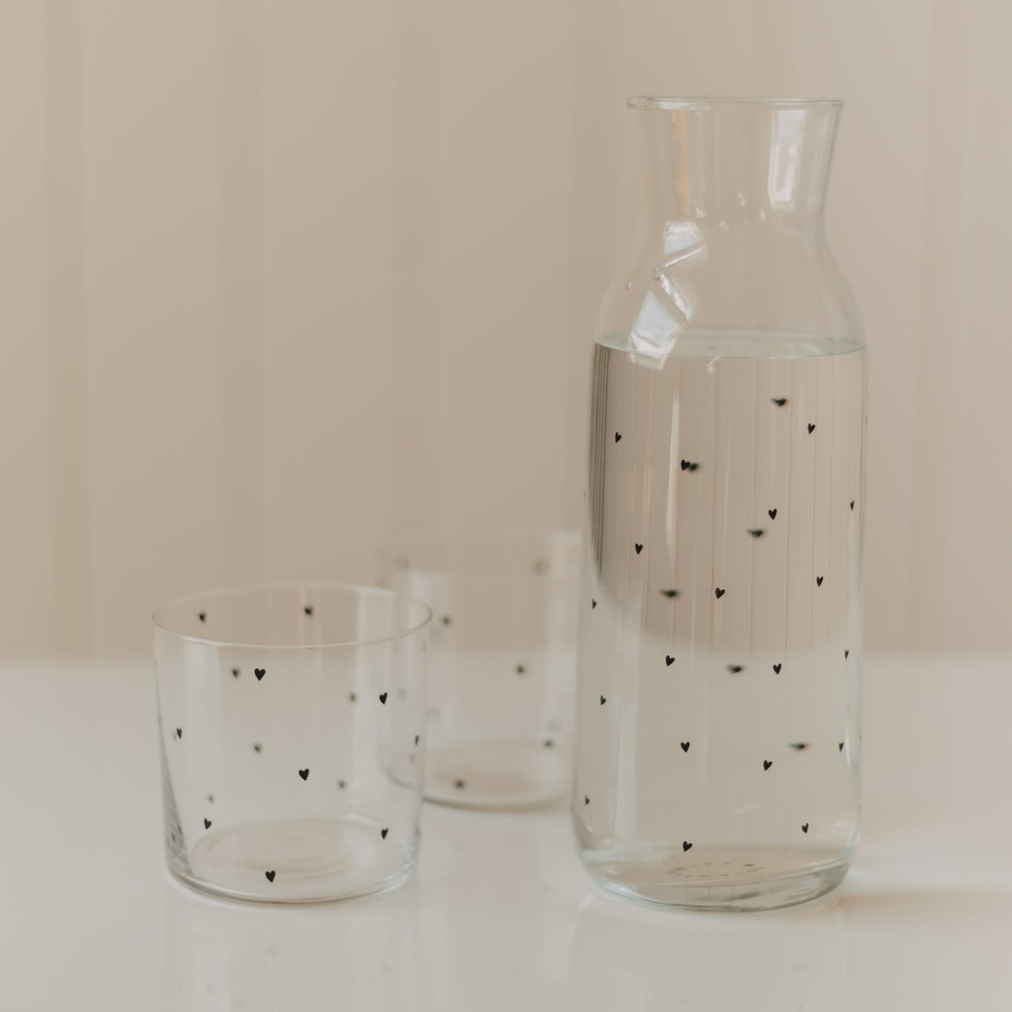 Glaskaraffe mit Wasser und zwei passenden Trinkgläsern mit kleinen schwarzen Herzen
