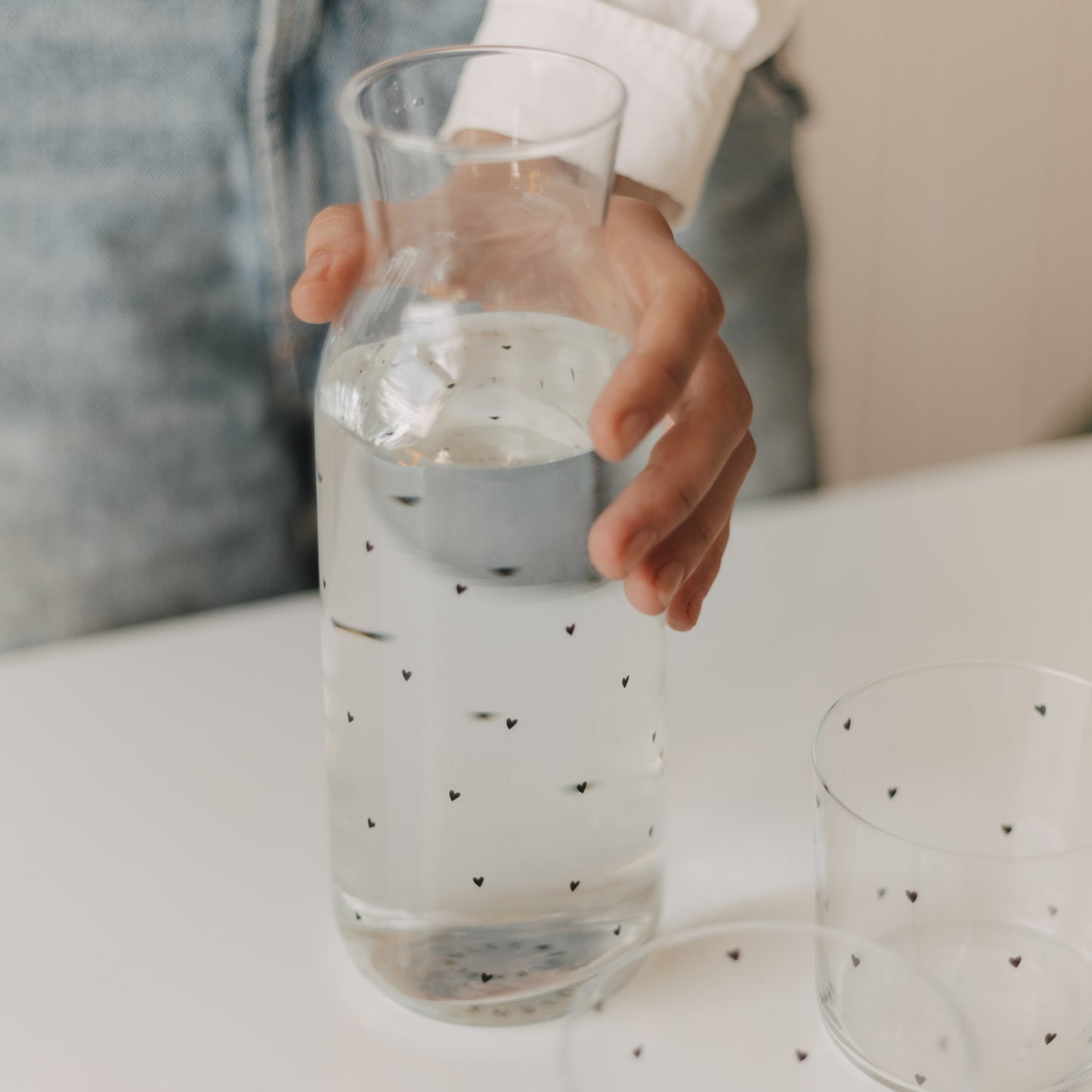 Hand hält eine mit Wasser gefüllte Glaskaraffe mit kleinen schwarzen Herzen