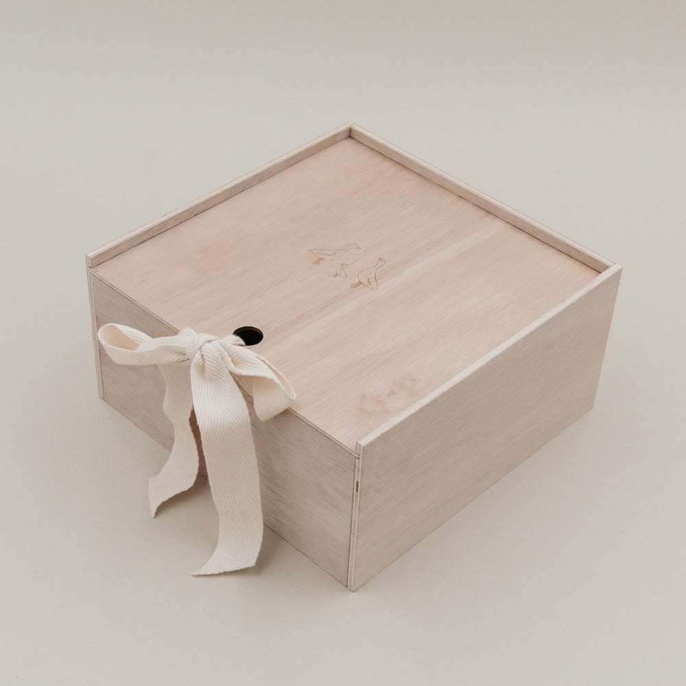 Erinnerungsbox aus hellem Holz mit Gänsegravur und Stoffschleife, frontal fotografiert.