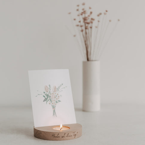 Dekorative Szene mit Holz-Kartenhalter „Heute ist dein Tag“, Teelicht und Blumenkarte im Hintergrund.