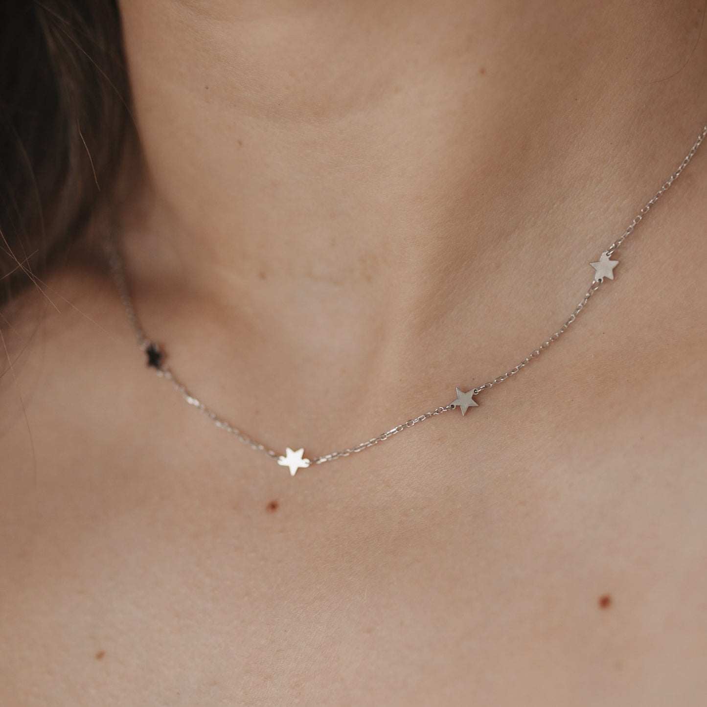Zarte silberne Kette mit kleinen Sternenanhängern getragen am Hals.