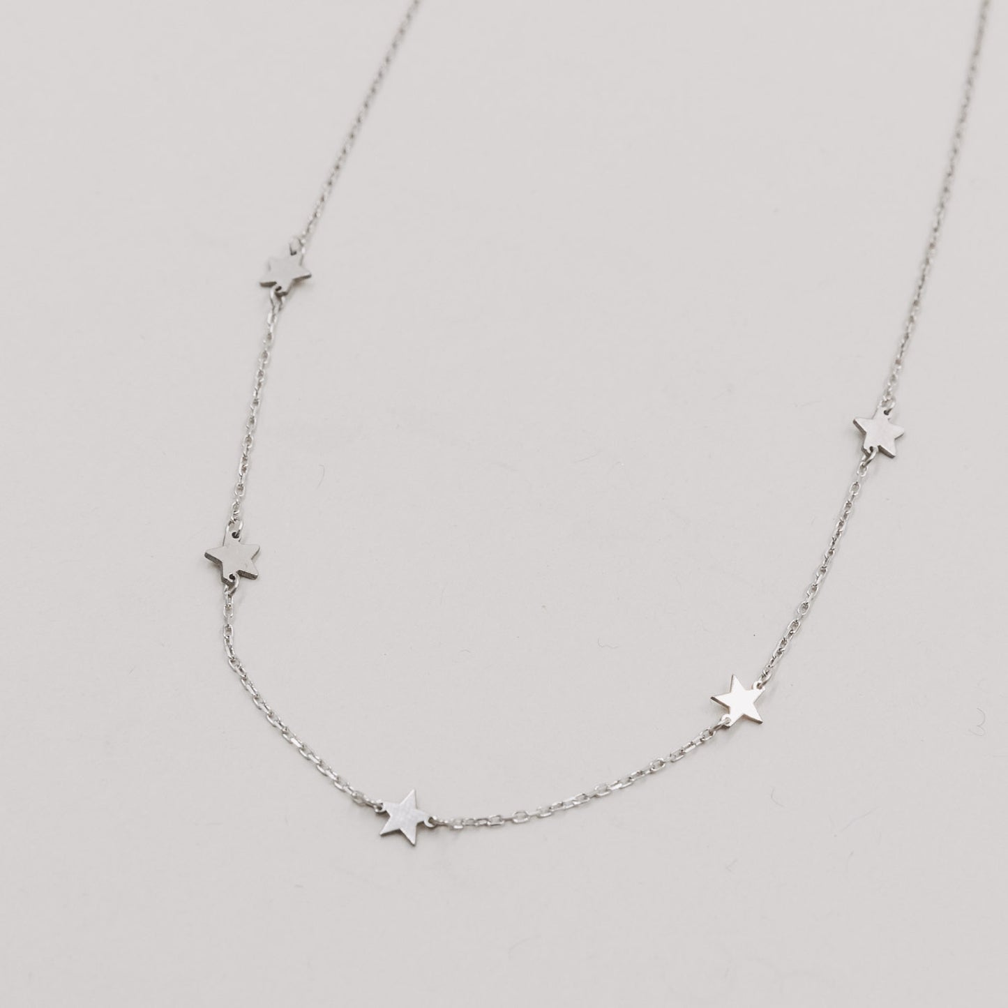 Silberne Kette mit kleinen, glänzenden Sternanhängern auf weißem Hintergrund.