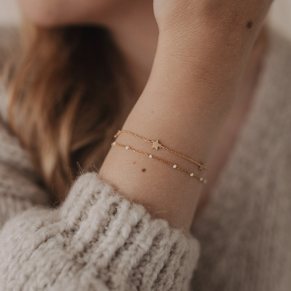 Zarte Kombination aus dem Armband Jackie Gold und einem zweiten Armband mit Perlendetails, am Handgelenk getragen.