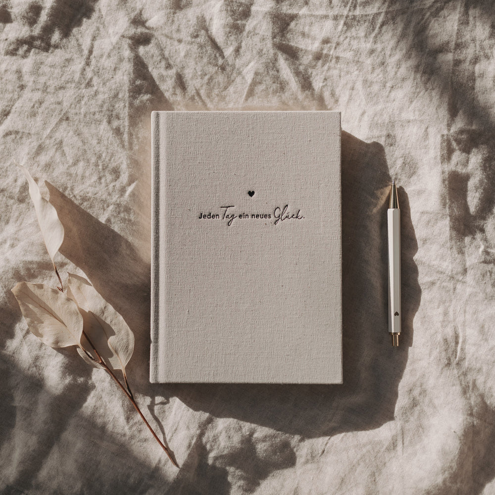 Undatierter Kalender Neues Glück mit Leinencover auf hellen Stofftüchern dekorativ arrangiert.