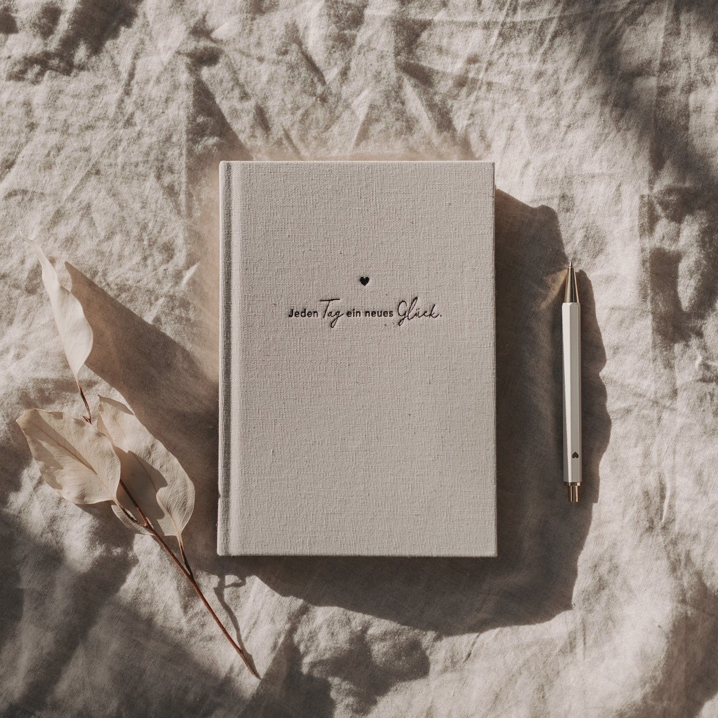 Undatierter Kalender Neues Glück mit Leinencover auf hellen Stofftüchern dekorativ arrangiert.