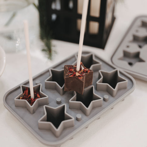 Sternform mit eingefüllter Trinkschokolade am Stiel, verziert mit Blüten, in winterlichem Setting.