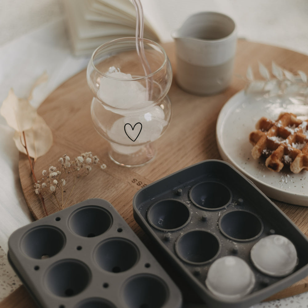 Geselliges Setting mit Eis-Kugeln im Glas, Form und Frühstücksaccessoires auf Holzplatte.
