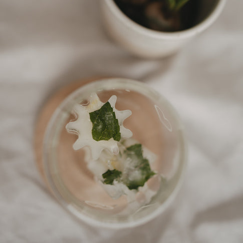 Fertiger Eiswürfel mit Minze aus der grauen Blütenform aus flexiblem Silikon gehalten in einem hohen Trinkglas.
