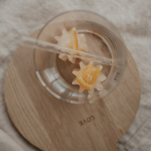 Fertiger Eiswürfel mit Orangenscheiben aus der grauen Blütenform aus flexiblem Silikon in einem Glas.