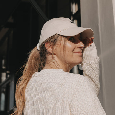 Frau trägt beige Cap mit schwarzem Herz-Stick und blickt über die Schulter