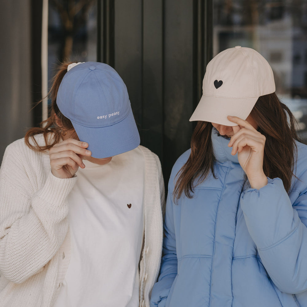 Zwei Frauen mit Caps: blaue „easy peasy“ Cap und beige Cap mit Herz-Stick