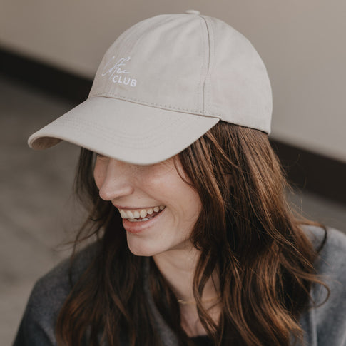 Frau trägt taupefarbene Cap „Coffee Club“ und lächelt