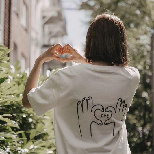 Frau formt Herz mit Händen, trägt T-Shirt mit LOVE-Print auf dem Rücken