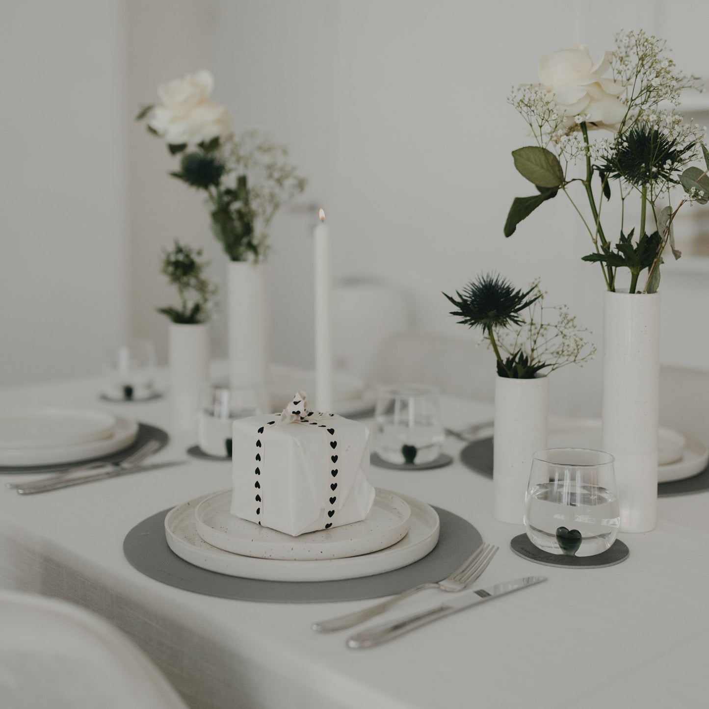 Tischdekoration mit grauem Platzset und weißem Geschirr sowie Geschenkpaket auf dem Teller.