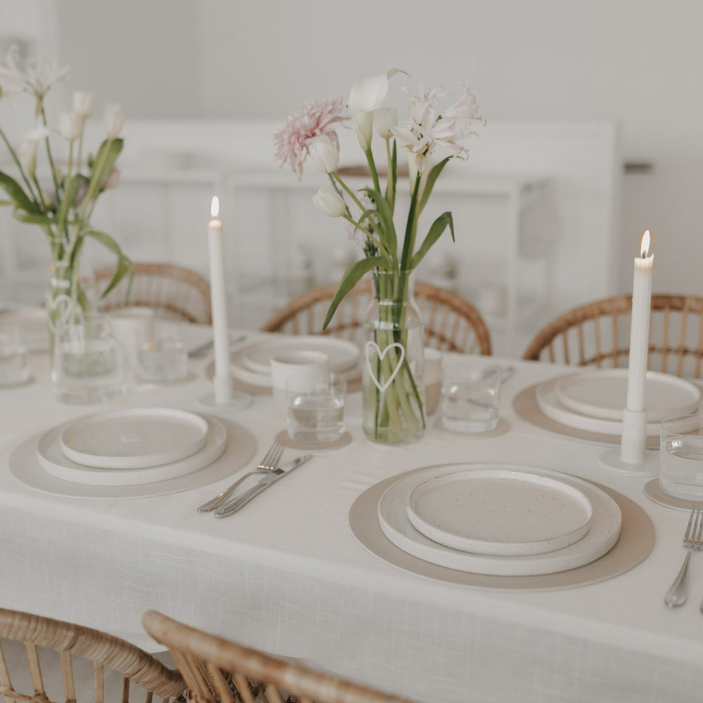 Hell gedeckter Tisch mit Blumen und rundem cremefarbenem Platzset mit Herzprägung von Eulenschnitt.