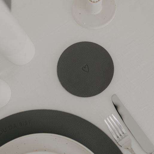 Wendbarer Untersetzer in Dunkelgrau mit eingeprägtem Herzmotiv auf gedecktem Tisch.