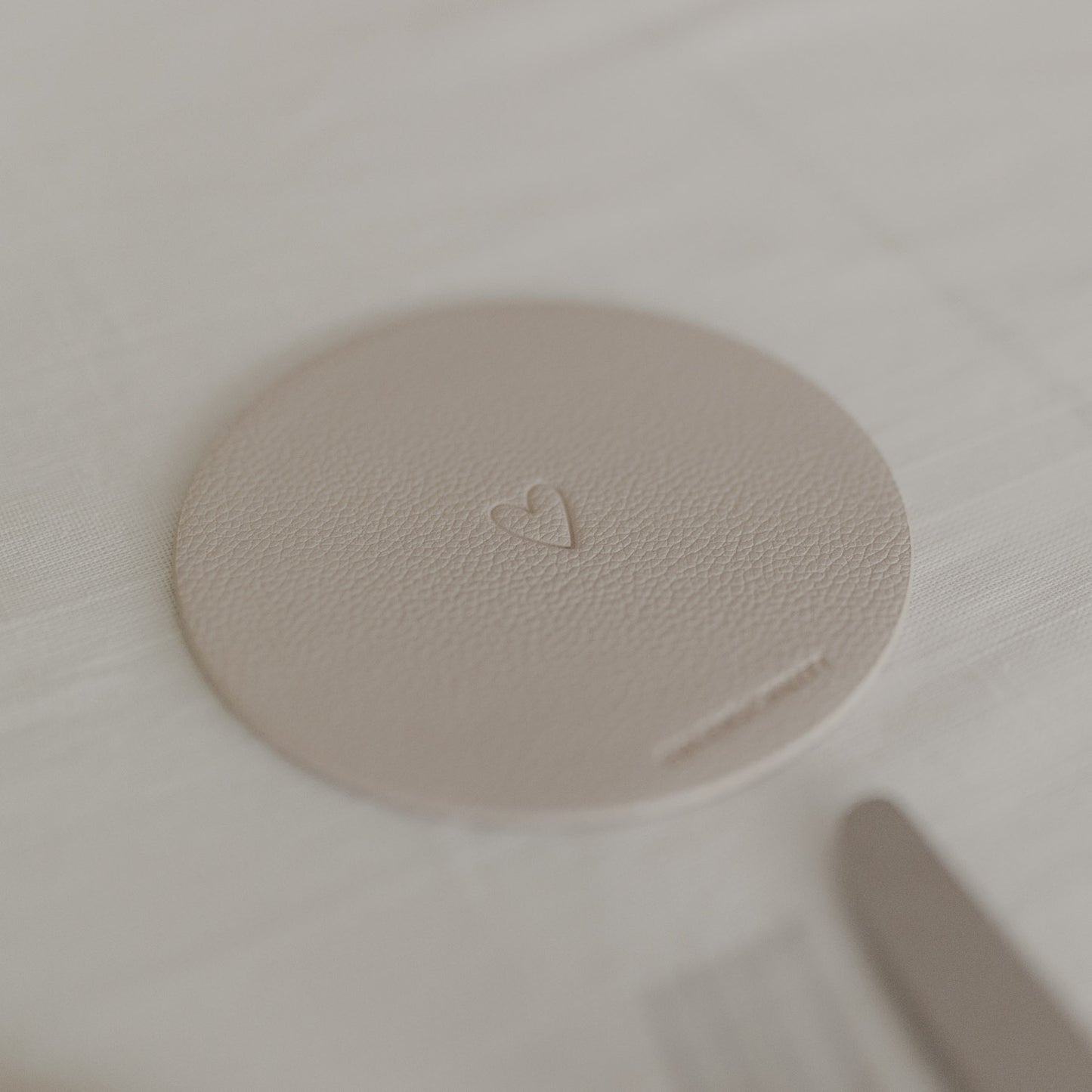 Runder cremefarbener Untersetzer mit geprägtem Herzmotiv auf weißer Tischdecke.