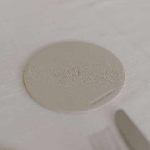 Runder cremefarbener Untersetzer mit geprägtem Herzmotiv auf weißer Tischdecke.
