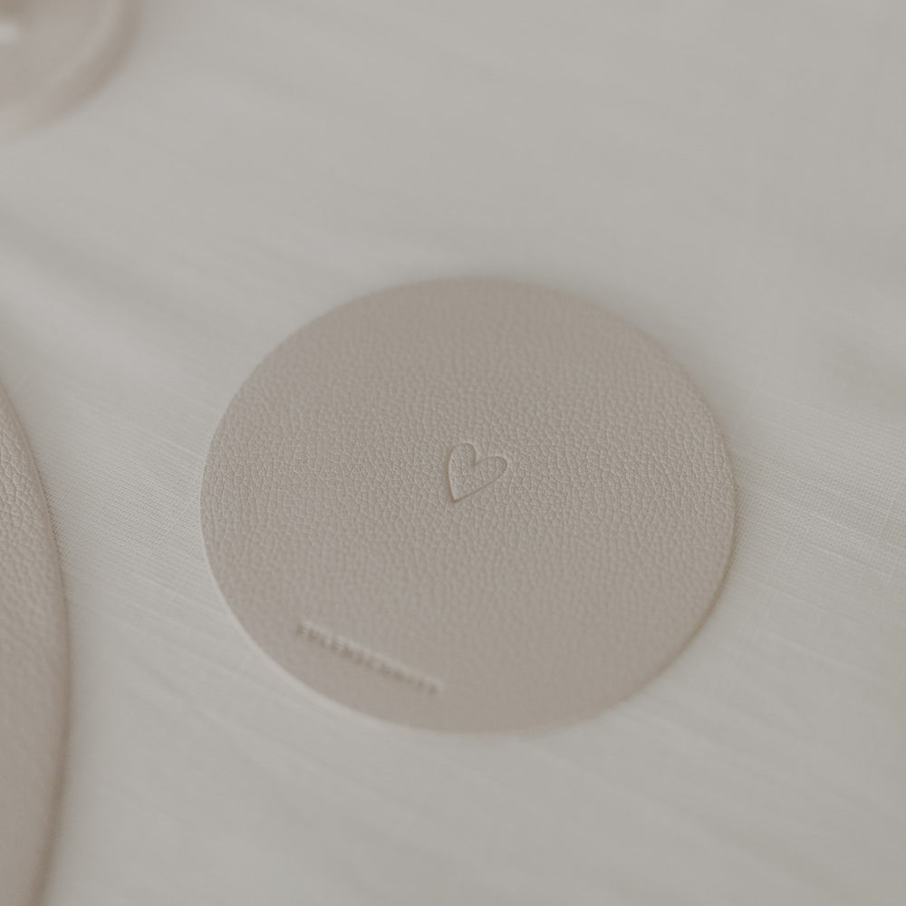 Cremefarbener Untersetzer mit geprägtem Herz neben Tischset und Besteck auf heller Tischdecke.