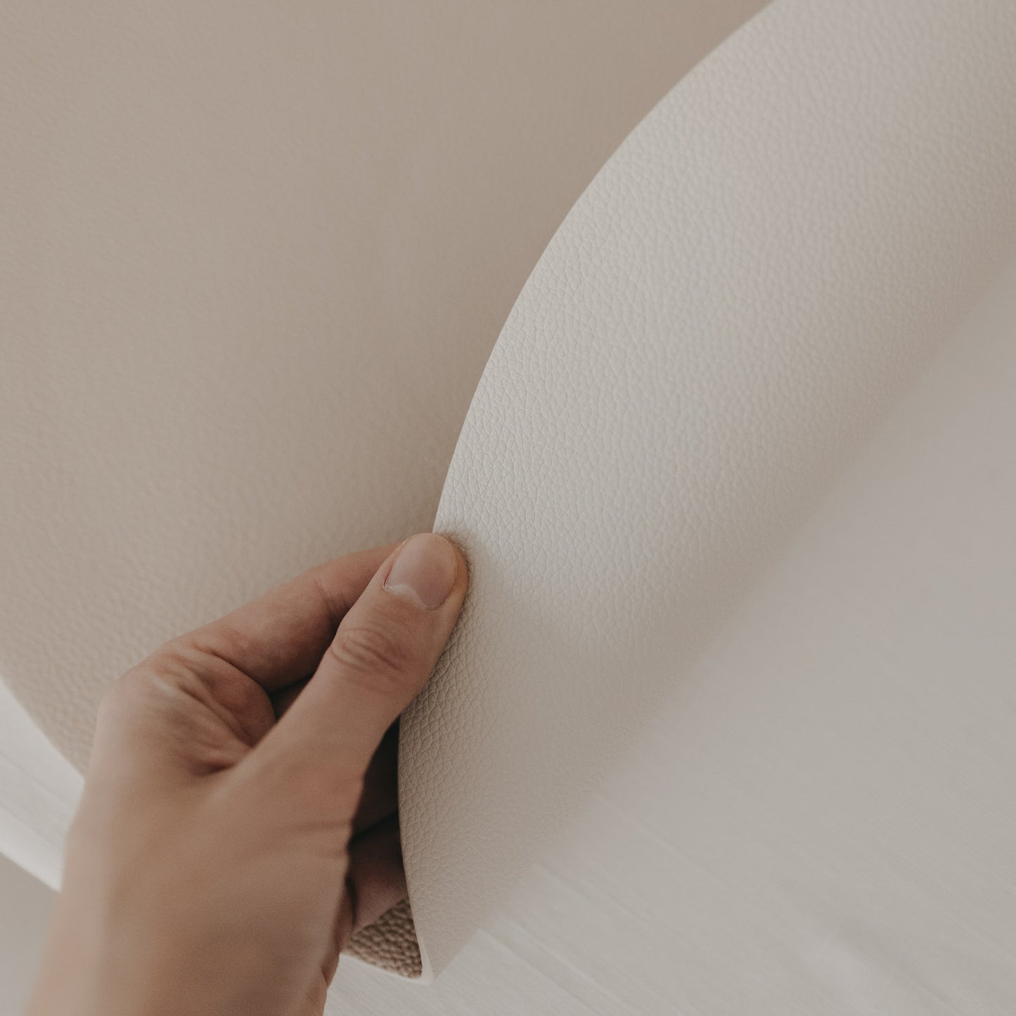 Wendbares cremefarbenes Platzset wird in der Hand gebogen und zeigt die strukturierte Oberfläche.