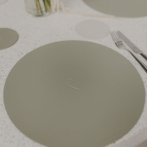 Helles grünes Platzset mit Herzprägung in Nahaufnahme auf Tischplatte.