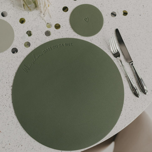 Grünes Platzset mit eingeprägtem Spruch ‚Wie schön, dass du da bist‘ neben Besteck auf gedecktem Tisch