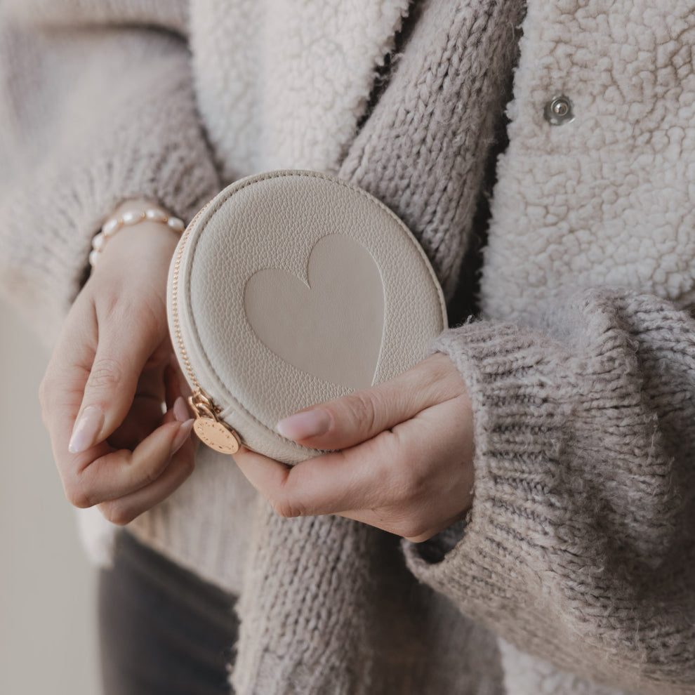 Cremefarbenes Herz-Portemonnaie in Händen mit goldenem Reißverschluss und rundem Münzetui-Design.