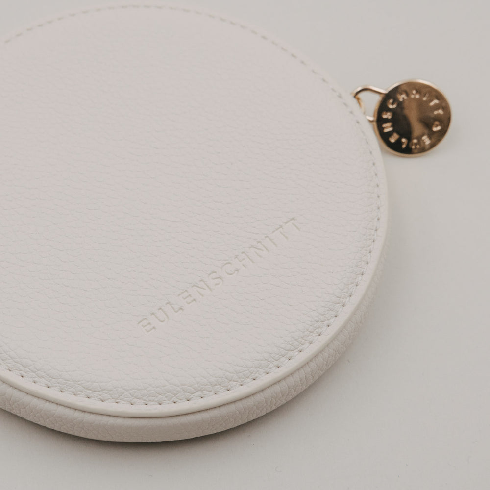 Rundes Portemonnaie in Creme mit geprägtem Eulenschnitt Logo und goldenem Reißverschlussanhänger.