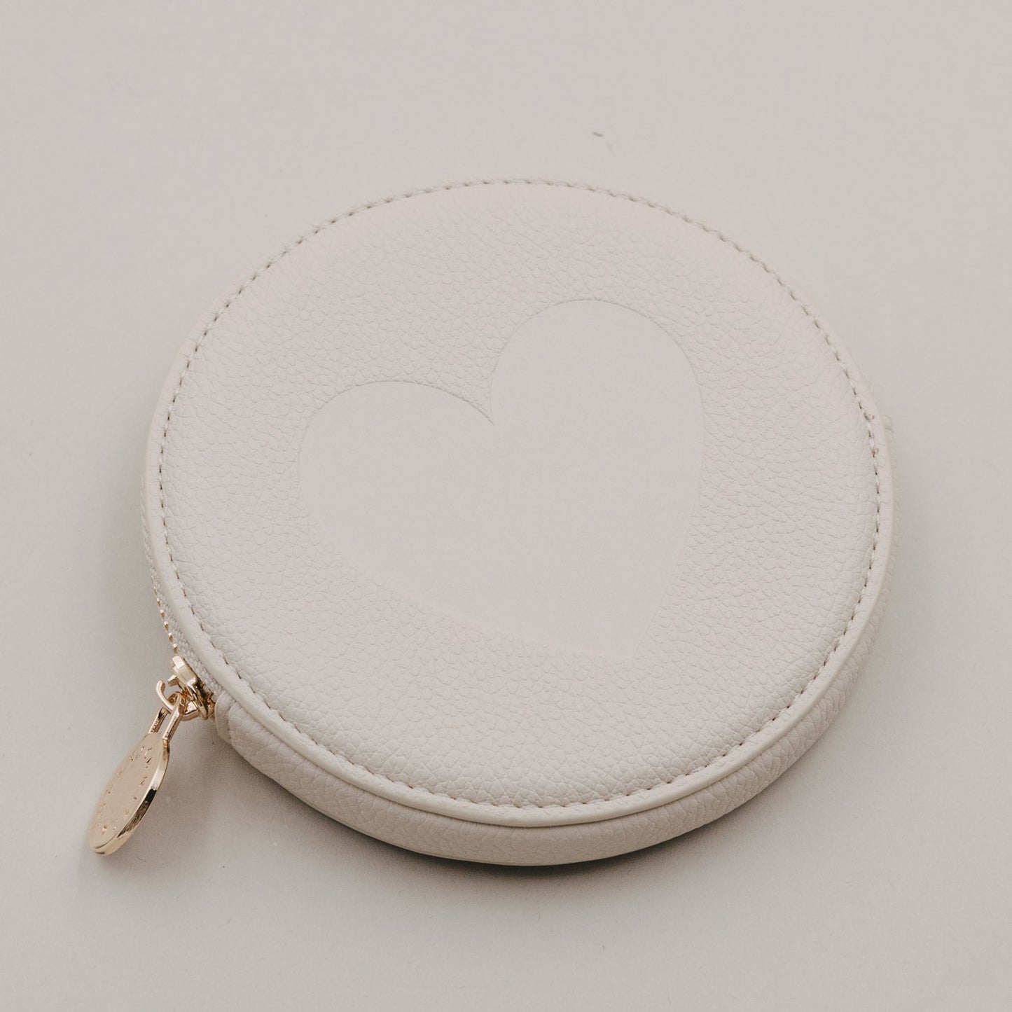 Rundes cremefarbenes Portemonnaie mit großem Herz auf der Vorderseite und goldenem Reißverschluss.