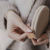 Beiges rundes Portemonnaie mit BOTOX MONEY Prägung, in Händen gehalten, goldener Zipperanhänger.