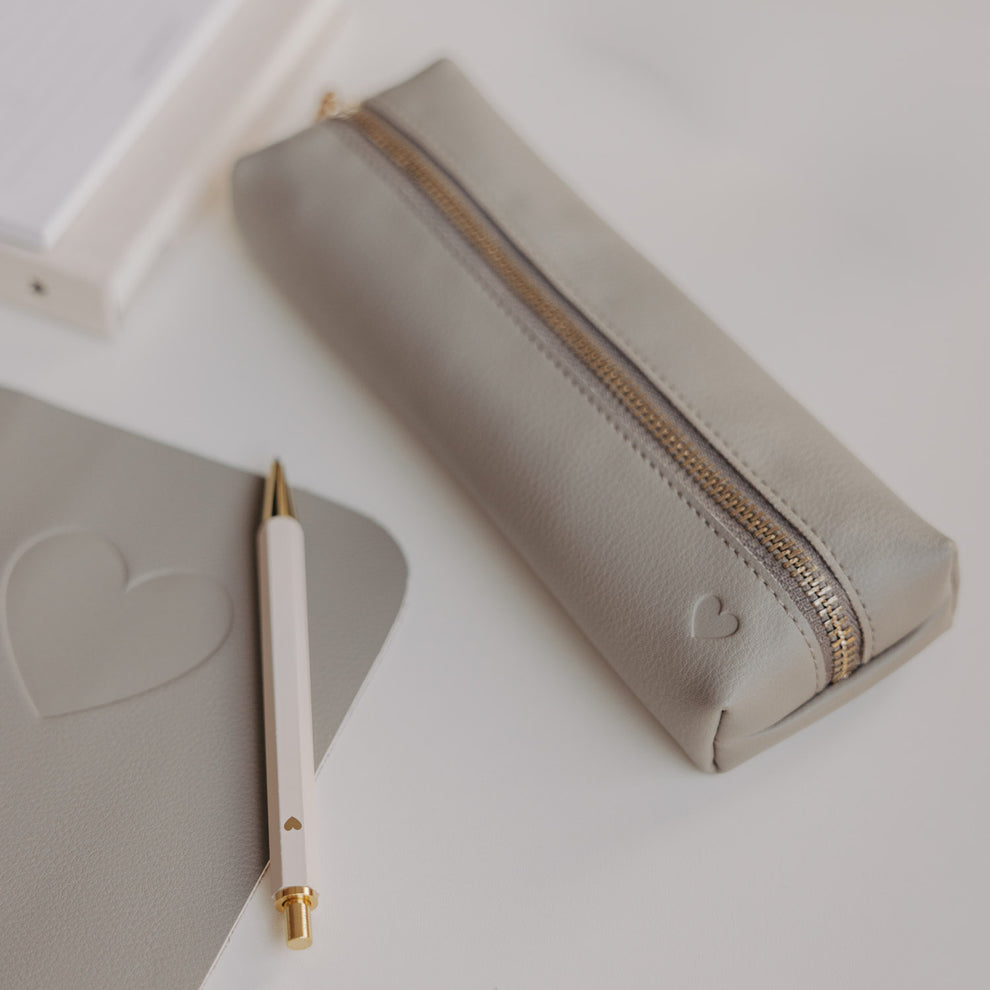 Graue Federtasche mit Herzprägung und goldenem Reißverschluss von Eulenschnitt neben Notizbuch und Stift