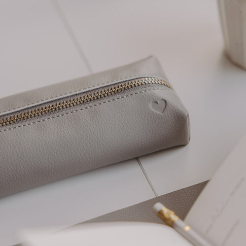 Graue Federtasche mit Herzprägung und goldenem Reißverschluss auf hellem Schreibtisch