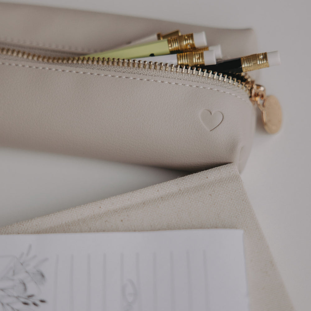 Federtasche taupe mit Herzprägung und Stiften im Inneren auf modernem Schreibtisch