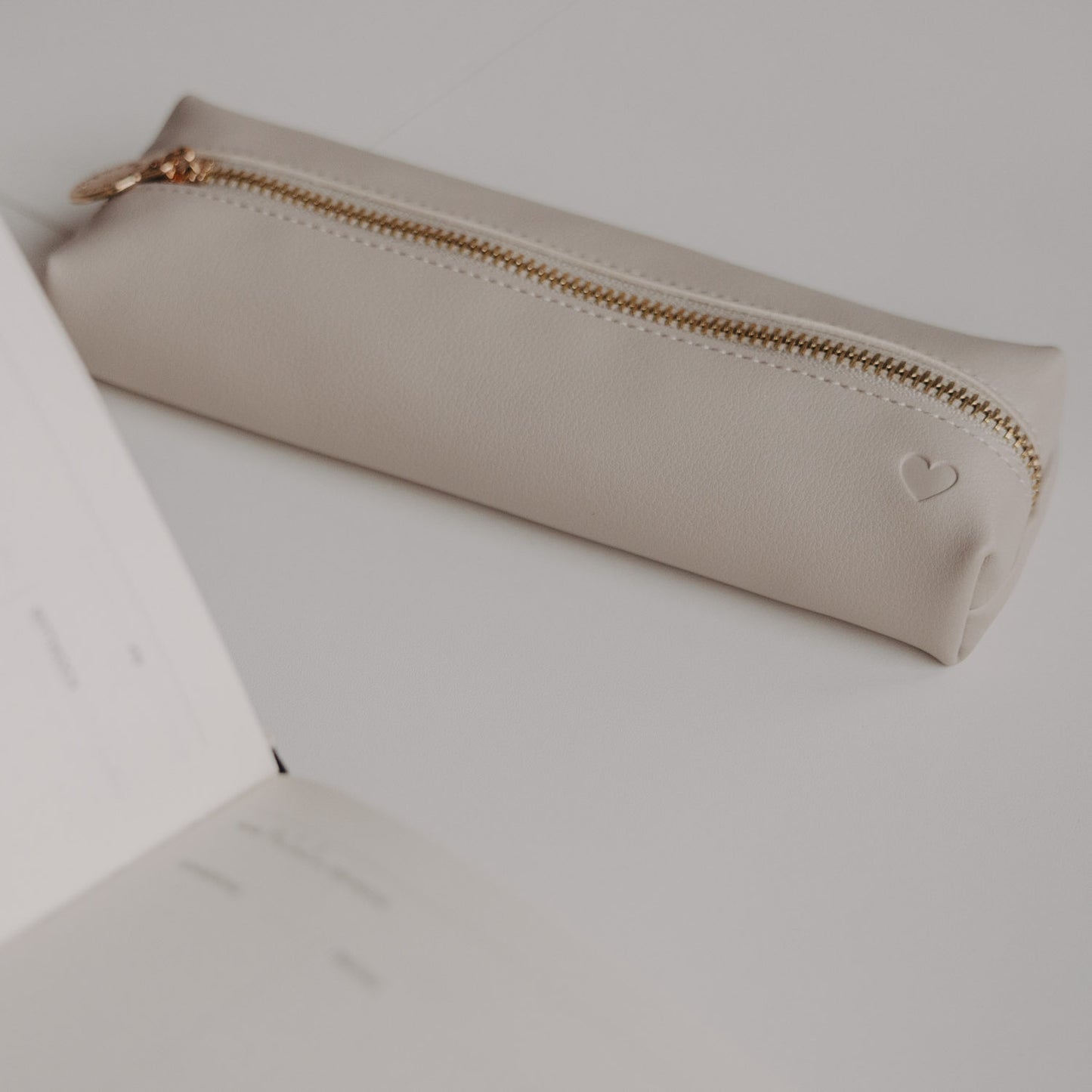Minimalistische Federtasche taupe mit Herzprägung von Eulenschnitt neben Notizbuch