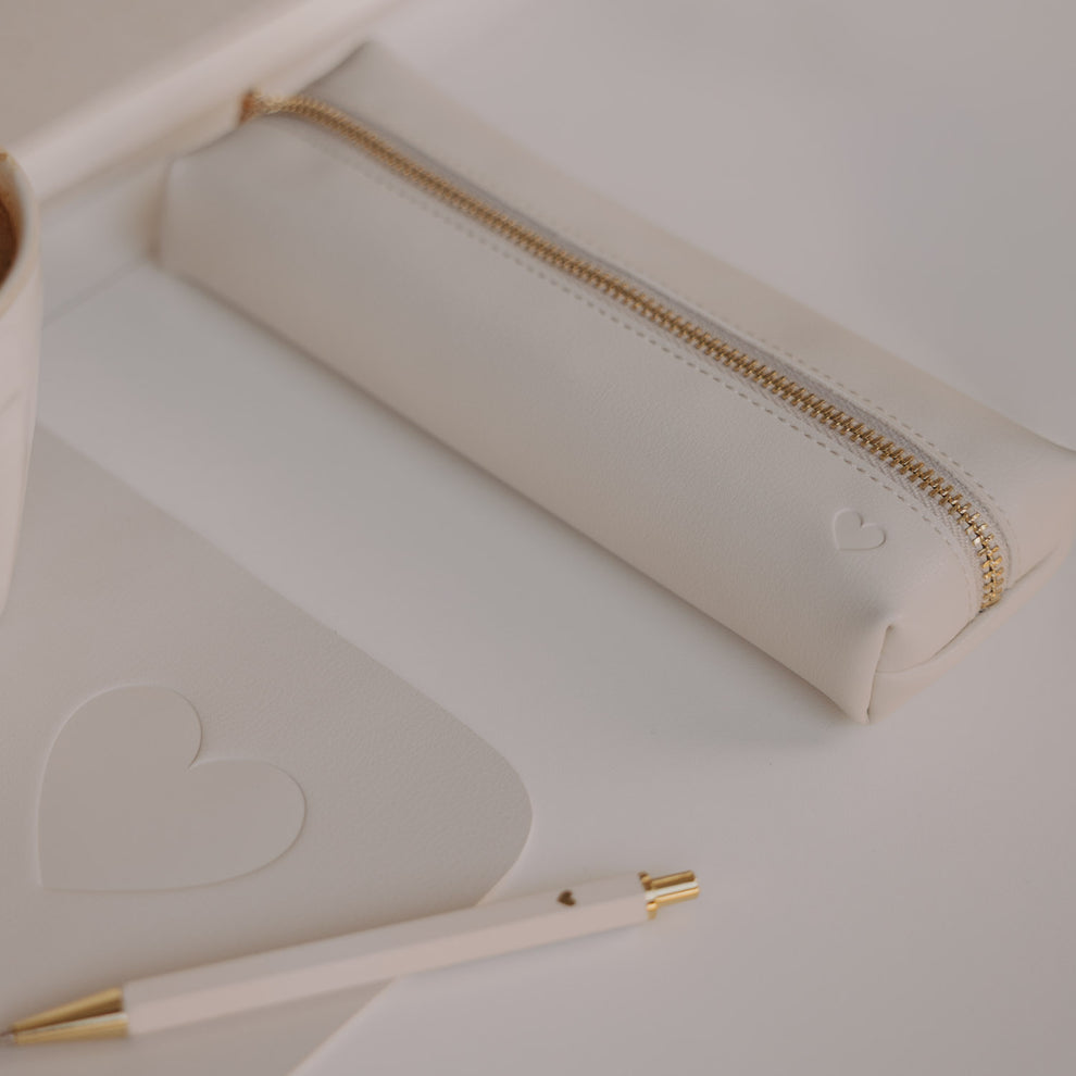Federtasche creme mit Herzprägung und goldenem Reißverschluss von Eulenschnitt neben Notizbuch und Stift