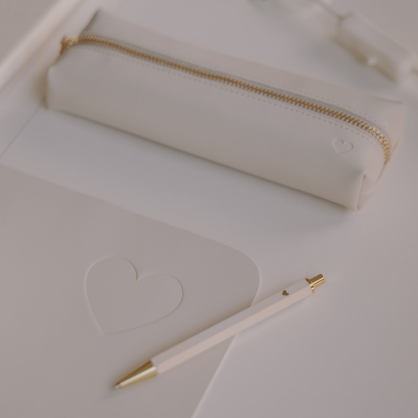 Federtasche creme mit Herzprägung auf Schreibtisch neben Notizbuch und Stift