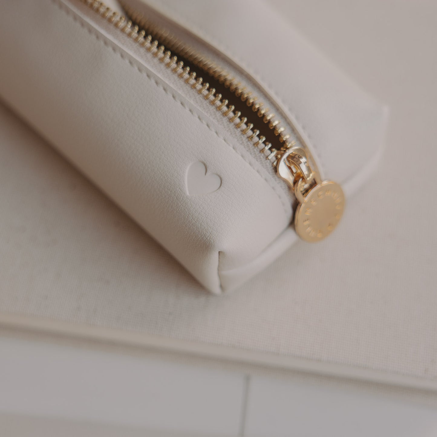 Detail der cremefarbenen Federtasche mit Herzprägung und goldenem Reißverschluss