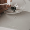 Glas mit schwarzem Herzdetail auf einem hellgrauen Untersetzer mit Herzprägung