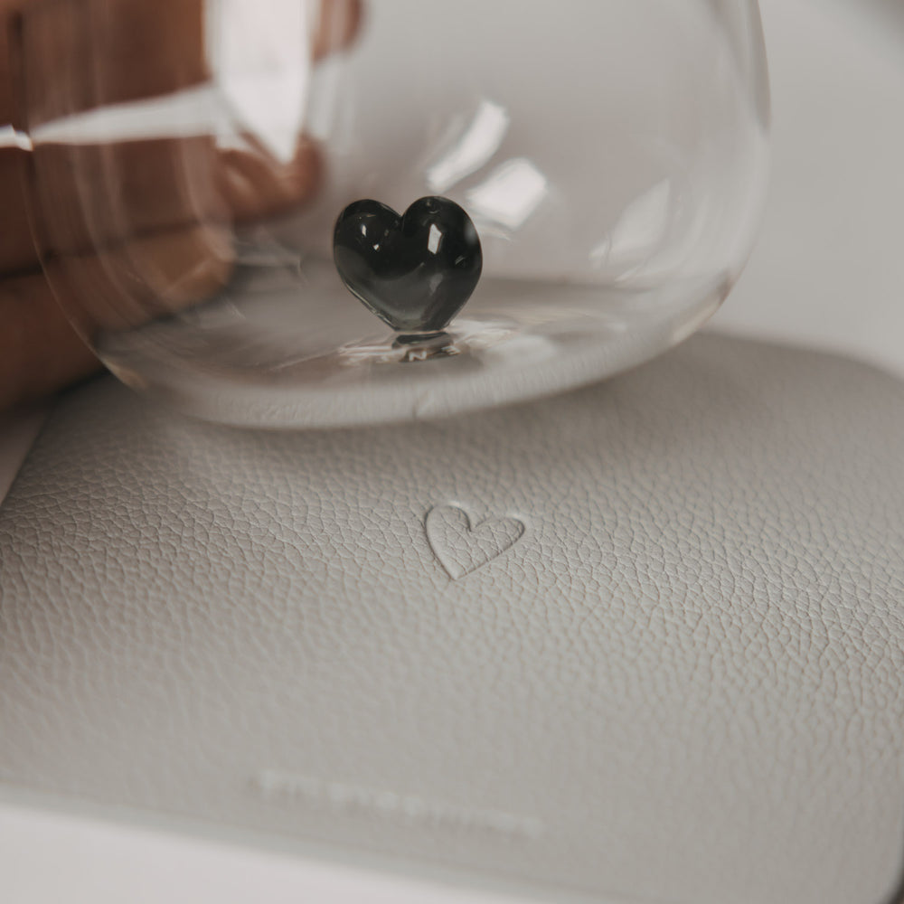Glas mit schwarzem Herzdetail auf einem hellgrauen Untersetzer mit Herzprägung