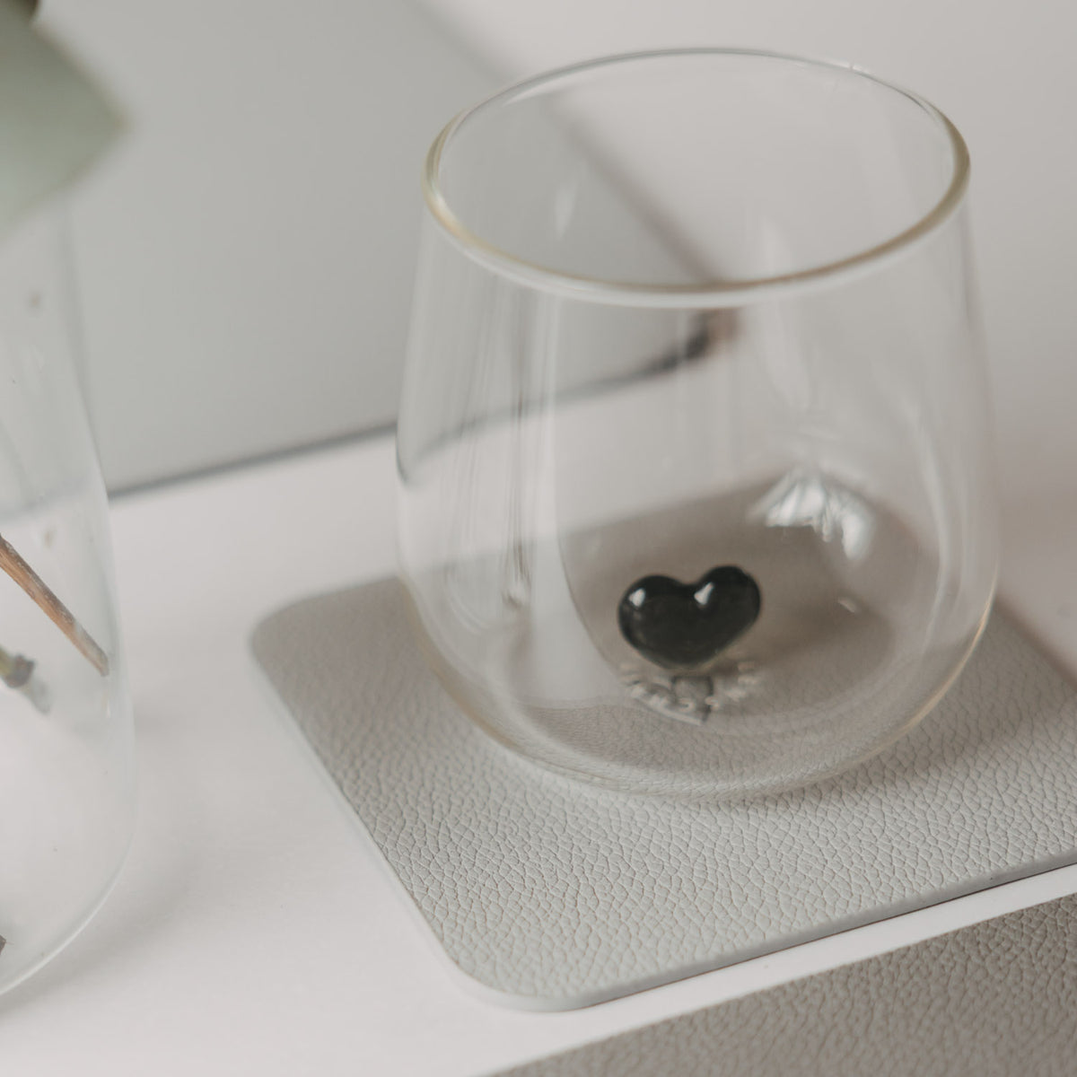 Hellgrauer eckiger Untersetzer mit Glas und schwarzem Herz als Detail
