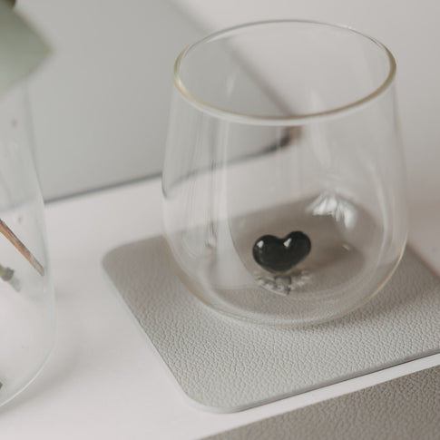 Hellgrauer eckiger Untersetzer mit Glas und schwarzem Herz als Detail