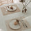 Zwei wendbare Platzsets in Creme und Beige mit Tellern, Besteck und Gläsern auf Esstisch
