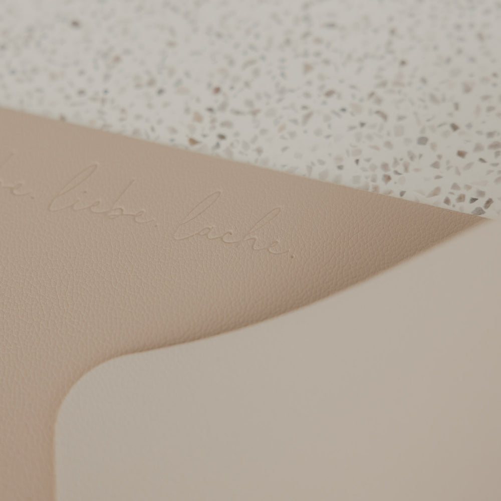 Detailaufnahme des beigen Platzsets in Lederoptik mit geprägtem Schriftzug „lebe liebe lache“