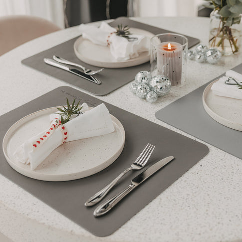 Graue wendbare Platzsets auf gedecktem Esstisch mit Tellern, Besteck und Kerze