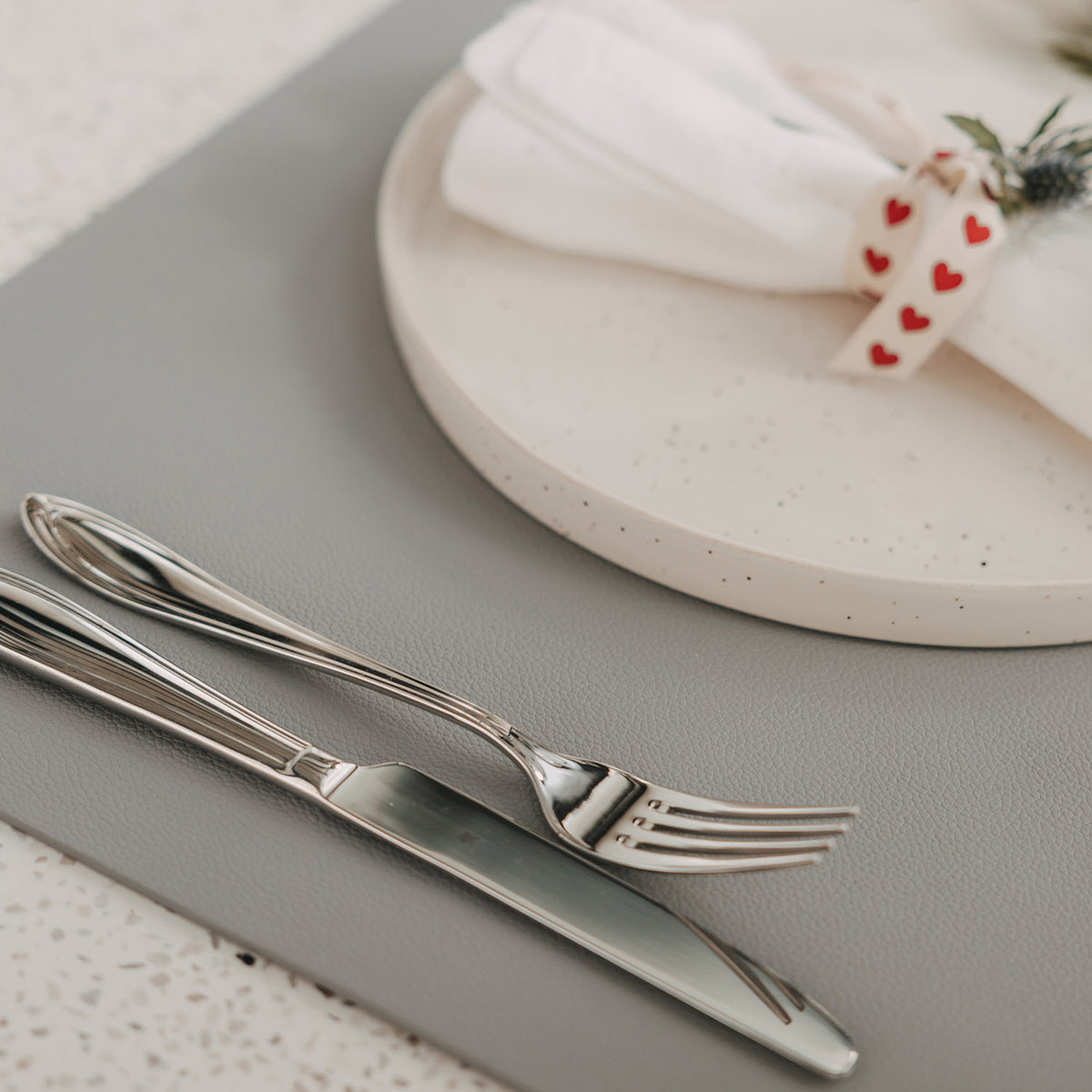 Graues Platzset in Lederoptik mit Teller, Serviette und Besteck auf gedecktem Tisch