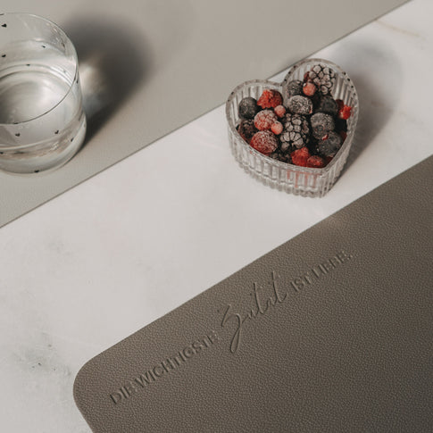 Dunkelgraues Platzset mit Prägung „Die wichtigste Zutat ist Liebe“ und Herzschale mit Beeren